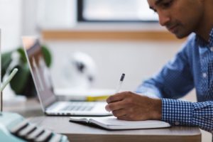 man with laptop doing research and making notes