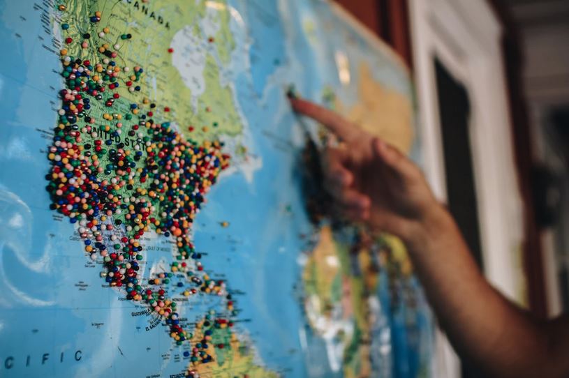 This photo shows someone pointing at a world map with pins highlighting different locations