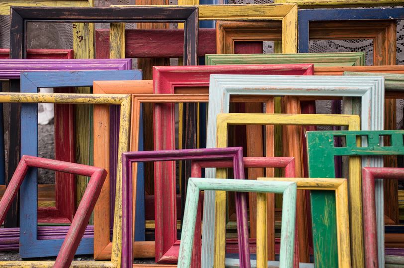 Image shows many different types of frames stacked up against a wall