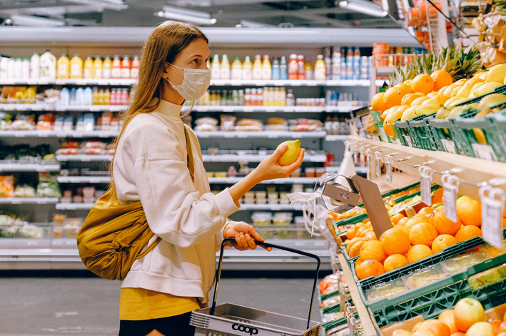 Image shows a woman doing her groceries while wearing a surgical mask on