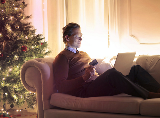 Holiday shopping: Man lounging on sofa with a laptop and credit card in hand.