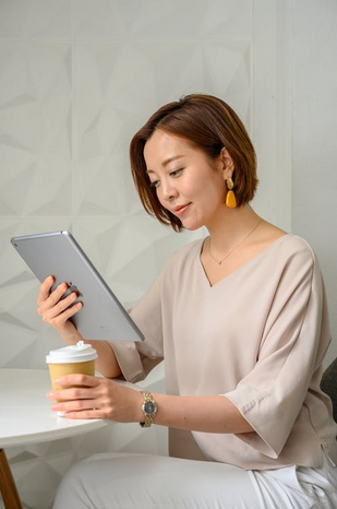 Woman holds a hot beverage in one hand and a tablet, that she is looking at, in the other.