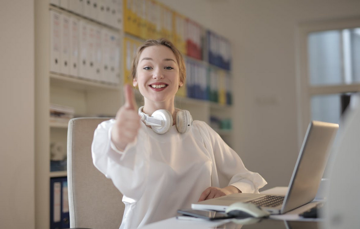 Woman in white gives a thumbs up from her office desk